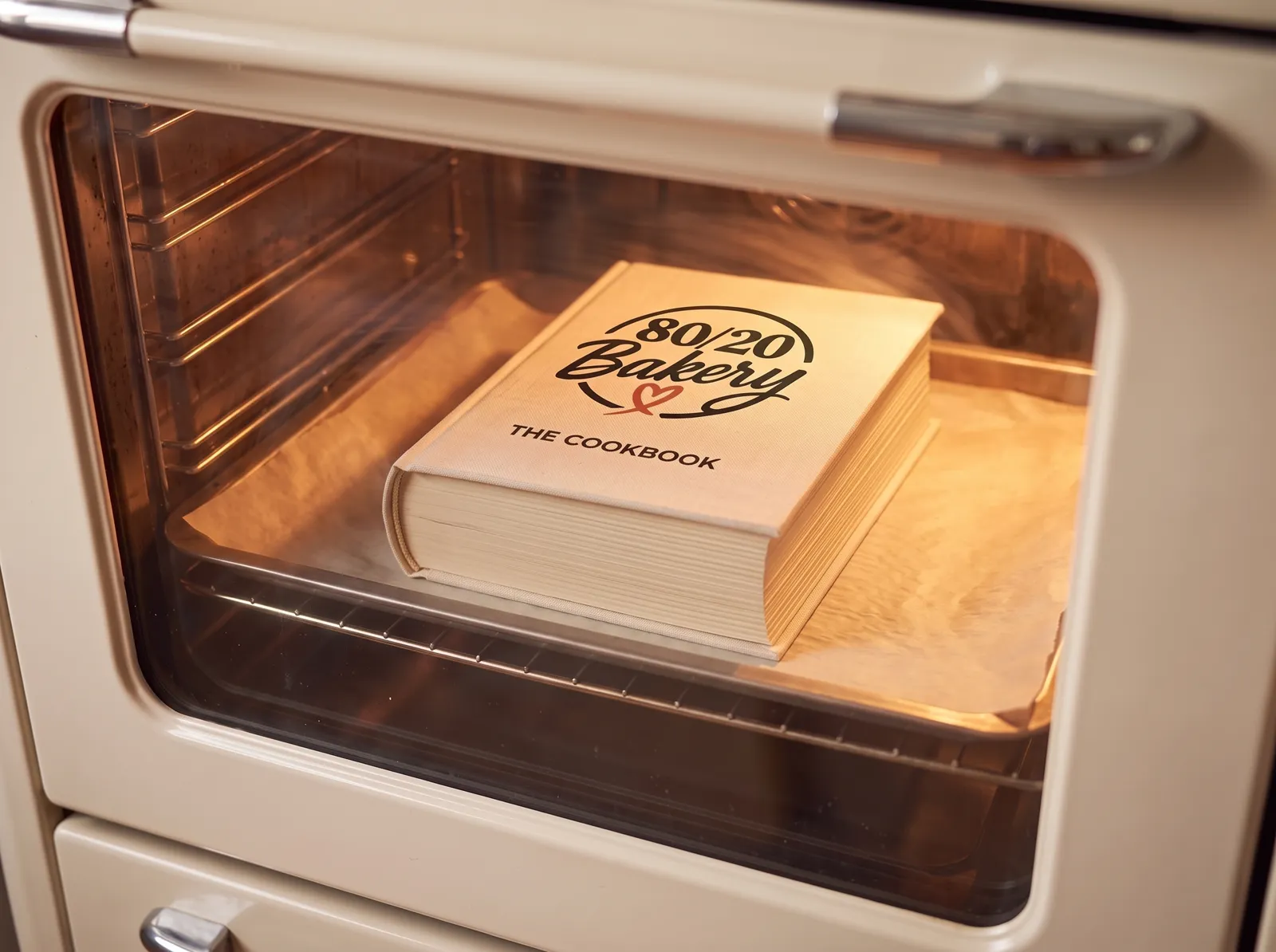 The 80/20 Bakery cookbook lying in a baking pan inside a glowing oven